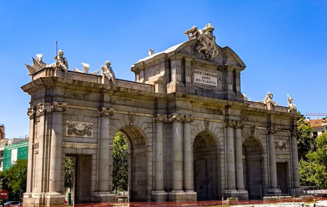 The Puerta de Alcalá in Madrid, a neoclassical granite monument with five arches and sculptural details under a blue sky in Madrid, Spain.